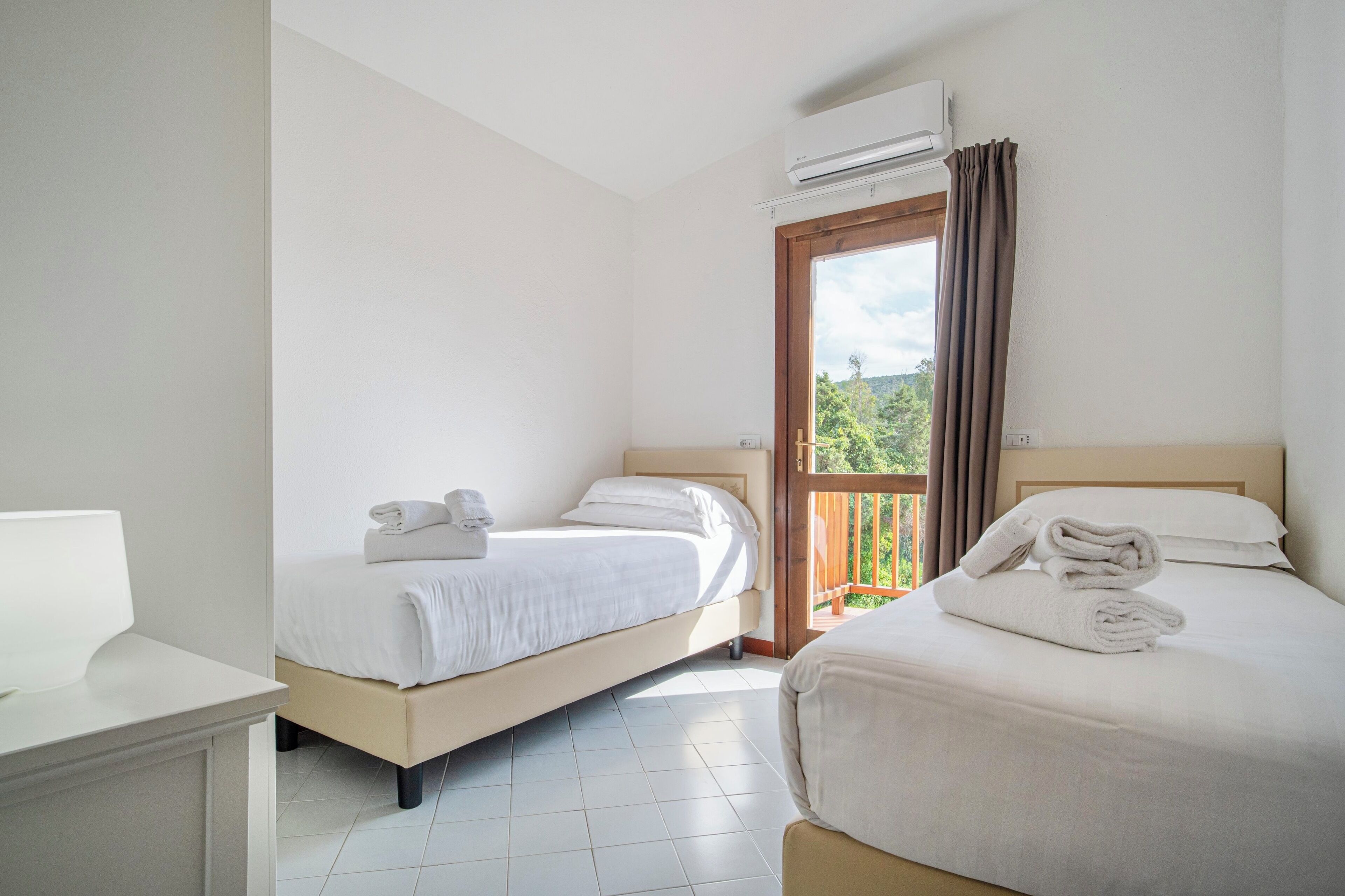 A hotel room with two beds, a balcony, and an air conditioning unit.