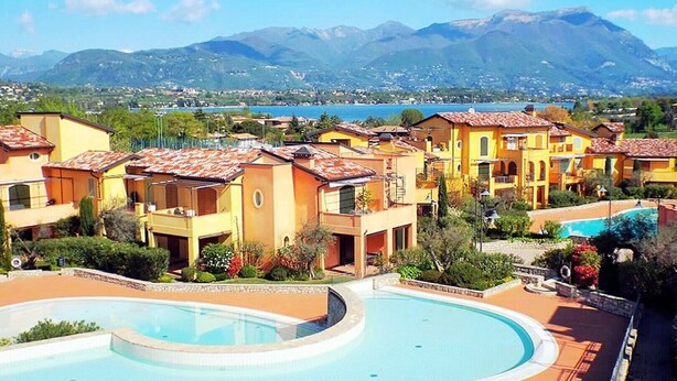 Ein Resort mit Gebäuden im mediterranen Stil, einem zentral gelegenen Schwimmbecken und einer gebirgigen Kulisse.
