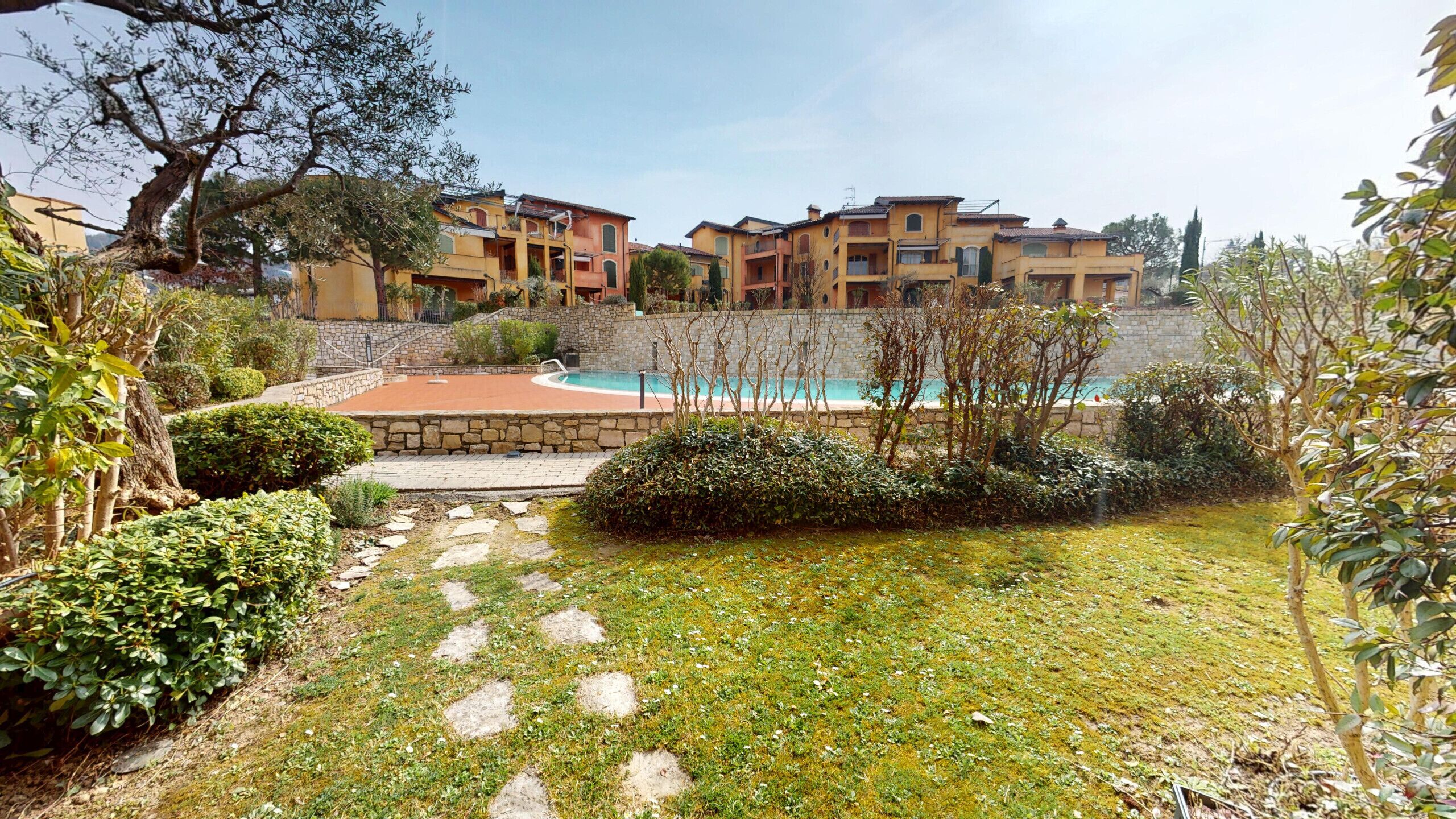 Un patio con piscina, un camino de piedra y edificios de varios pisos al fondo.