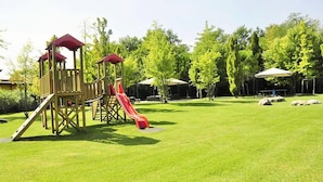 Ein Spielplatz mit einer Holzrutsche und Klettergerüsten, umgeben von einem gepflegten Rasen und Bäumen.