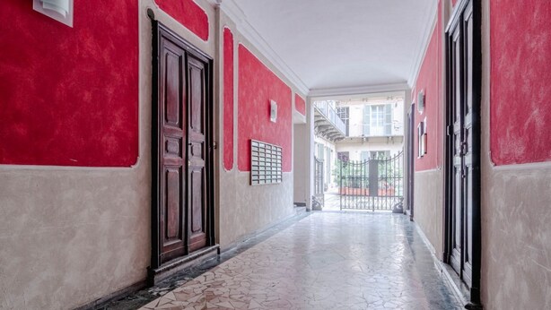 A corridor with red walls, a tiled floor, and a door with a metal gate. - GuestHost - A comfortable, welcoming 40 square meters apartment, perfect for four people, located on the second floor of a period building (NO elevator).The property is located near the Vittorio Emanuele I Bridge in a quiet residential area, well-connect (Turin)