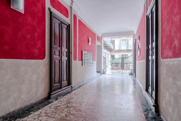 Un pasillo con paredes rojas, piso de baldosas y una puerta con reja de metal.