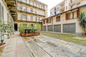 Un patio con suelo de piedra, plantas en macetas y un edificio con múltiples balcones y ventanas.