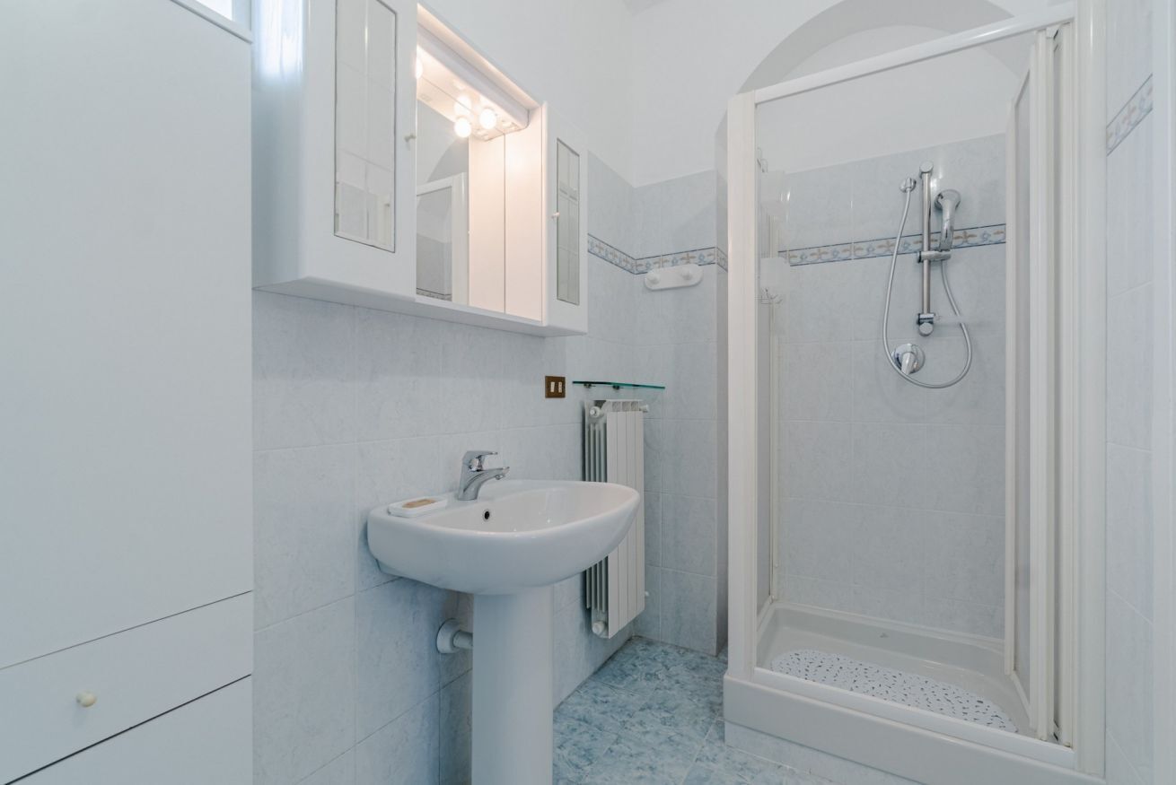 Ein Badezimmer mit einem weißen Waschbecken, einem Spiegel, einer Duschkabine und Fliesenboden.