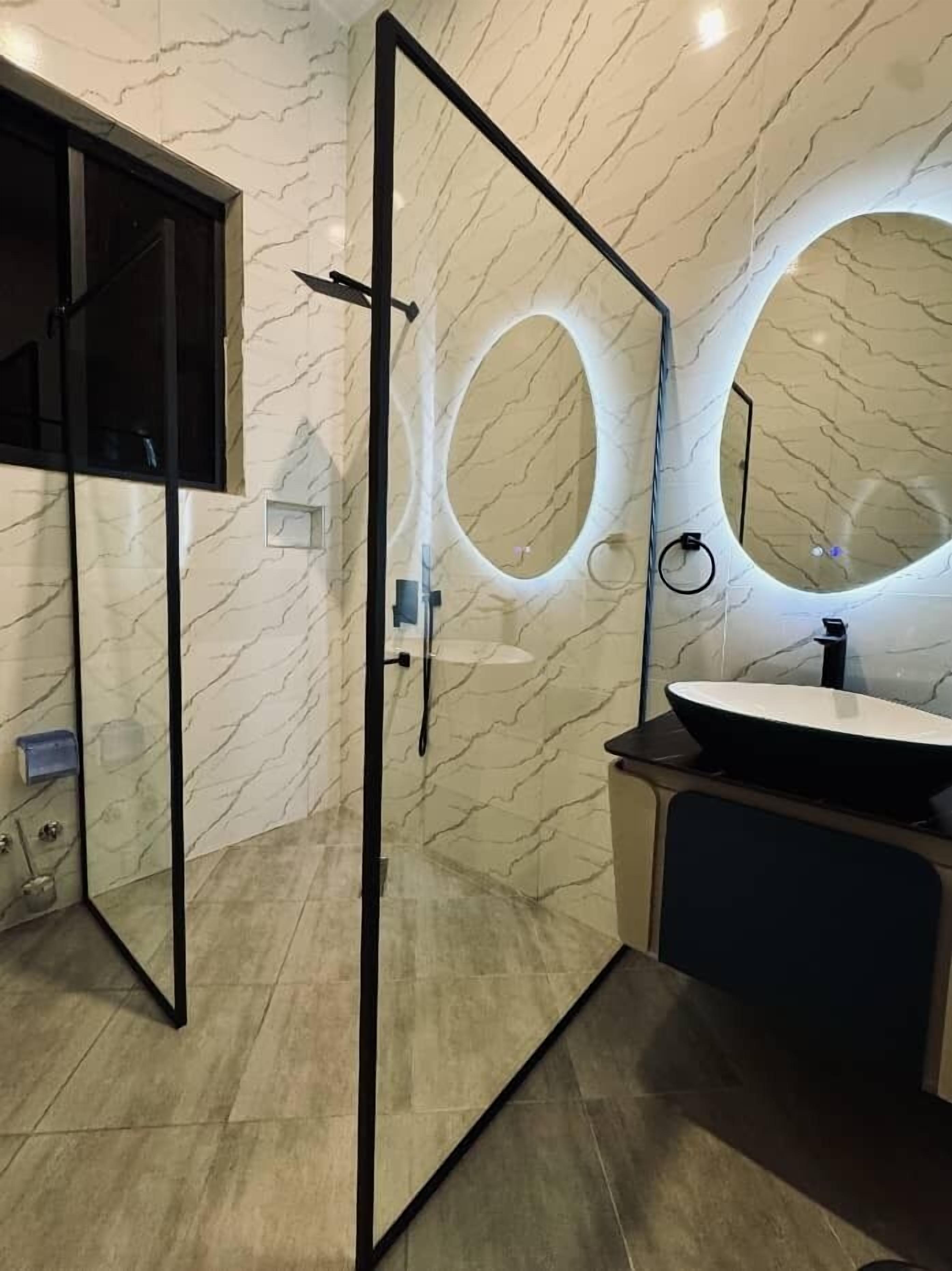 Une salle de bain moderne avec une douche à l’italienne en verre, un grand miroir rond et un grand lavabo.