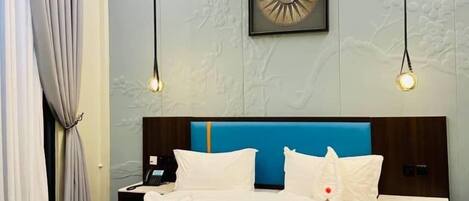 A modern hotel room with a large bed, a nightstand, a desk, and a wall-mounted artwork.