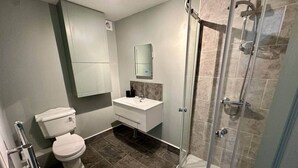 Baño con inodoro, lavamanos, espejo, ducha y piso de baldosas.