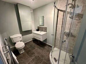 Baño con inodoro, lavamanos, espejo, ducha y piso de baldosas.