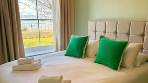 Una cama con cabecera acolchada, dos almohadas verdes y dos toallas blancas dobladas.