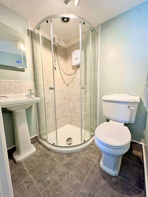 Un bany amb dutxa de vidre, un lavabo pedestal i un vàter.