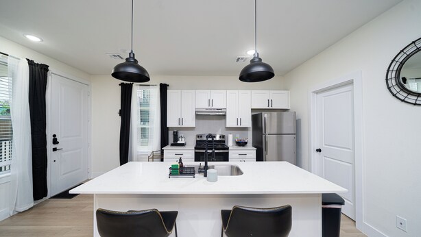 A modern kitchen with white cabinets, a central island, two black chairs, and pendant lighting. - Cozy East Downtown Houston Getaway Near UH, Med Center, NRG Stadium (Houston)