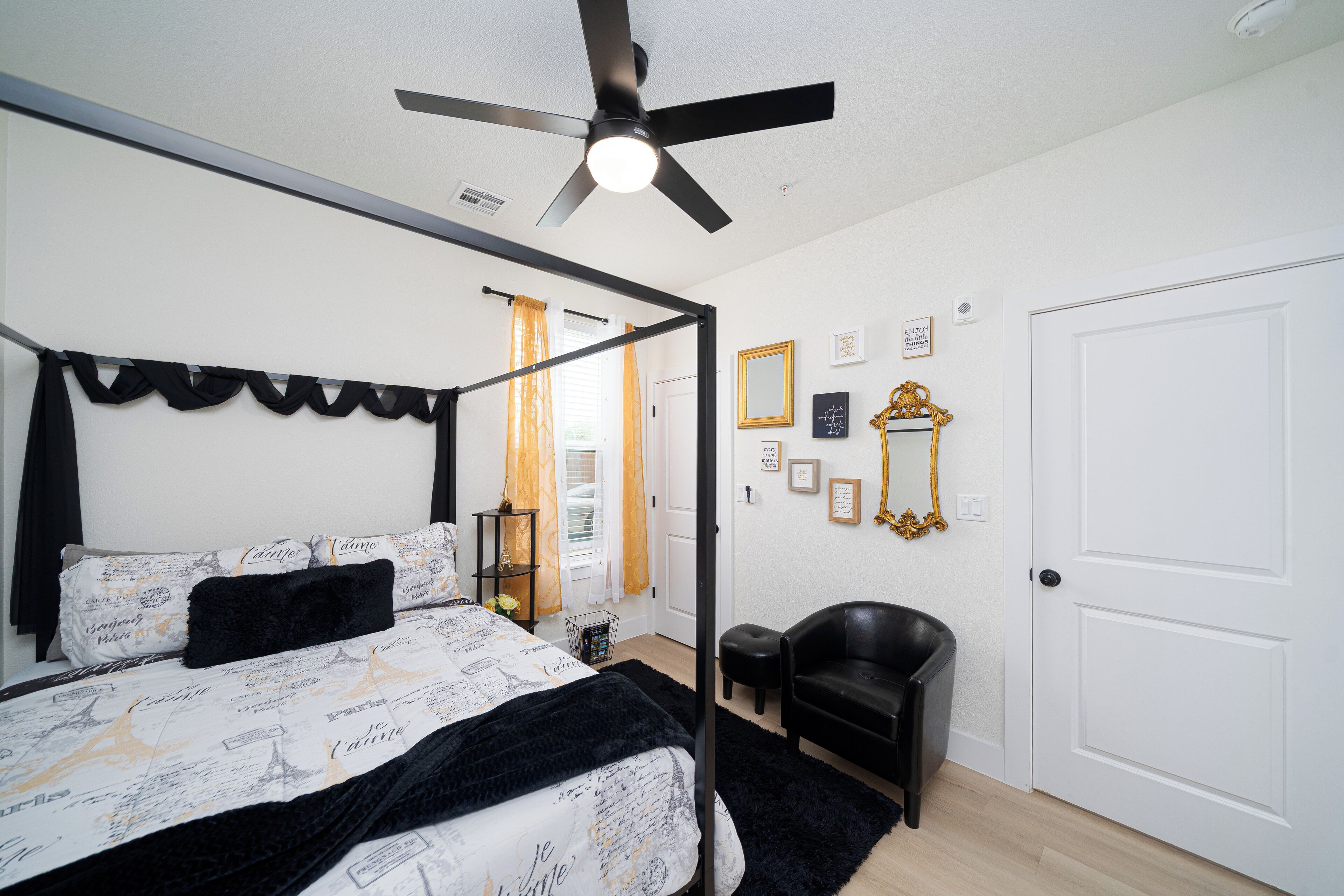 A bedroom with a four-poster bed, a ceiling fan, a black leather chair, and a white door.