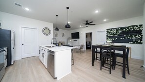 A modern kitchen with white cabinets, a central island, and a dining area with a black table and chairs. - Cozy East Downtown Houston Getaway Near UH, Med Center, NRG Stadium (Houston)