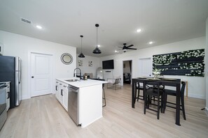 A modern kitchen with white cabinets, a central island, and a dining area with a black table and chairs. - Cozy East Downtown Houston Getaway Near UH, Med Center, NRG Stadium (Houston)