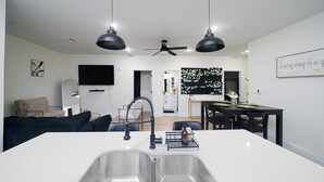 A modern kitchen with a central island, a dining area with a dark table, and a living space with a sofa and a TV. - Cozy East Downtown Houston Getaway Near UH, Med Center, NRG Stadium (Houston)
