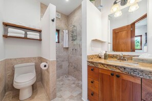 Une salle de bain comprenant des toilettes, une douche et un meuble-lavabo avec un évier et un miroir.