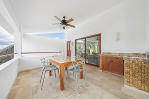 Ein Balkon mit Tisch und Stühlen, Deckenventilator, eine Schiebetür und ein Küchenbereich mit Spüle und Arbeitsplatte.