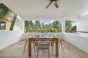 A dining area with a table and chairs, a ceiling fan, and a view of palm trees. - Stylish, new apartment in Sac Bajo w/private dock (Isla Mujeres)
