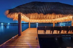 A wooden deck leading to a thatched-roof structure with seating, overlooking calm water. - Stylish, new apartment in Sac Bajo w/private dock (Isla Mujeres)