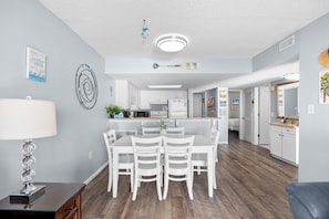 A modern kitchen with white cabinets, a central island, and a dining area with white chairs. - Waterpointe II 704 - Spacious 3 Bedroom Condo (North Myrtle Beach)