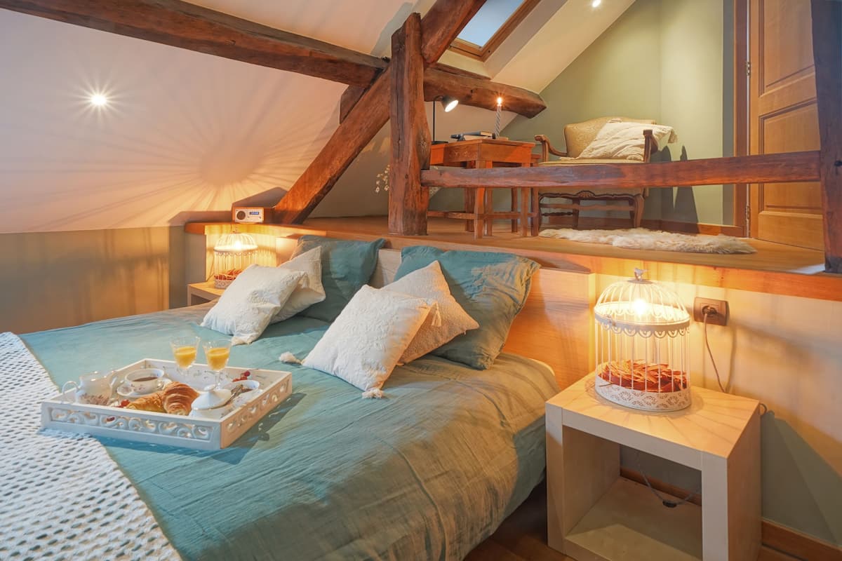 Un dormitorio acogedor con cama en altillo, una mesita de noche con un farol y una bandeja de desayuno sobre la cama.