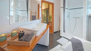 Un baño moderno con un espejo grande, un lavabo blanco, un mueble de tocador de madera, una bañera y una zona de ducha.