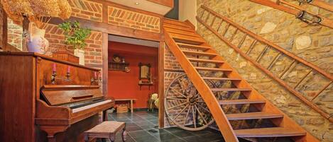 Un piano de cola, una escalera de madera y una gran rueda de madera en una habitación con paredes de ladrillo y piso de piedra.