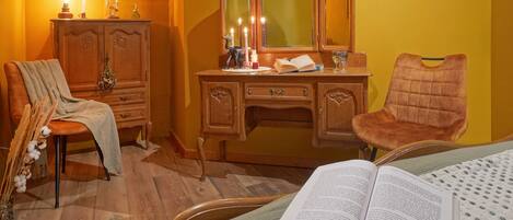 A room with a wooden dresser, a chair, a bed with an open book, and a lamp.
