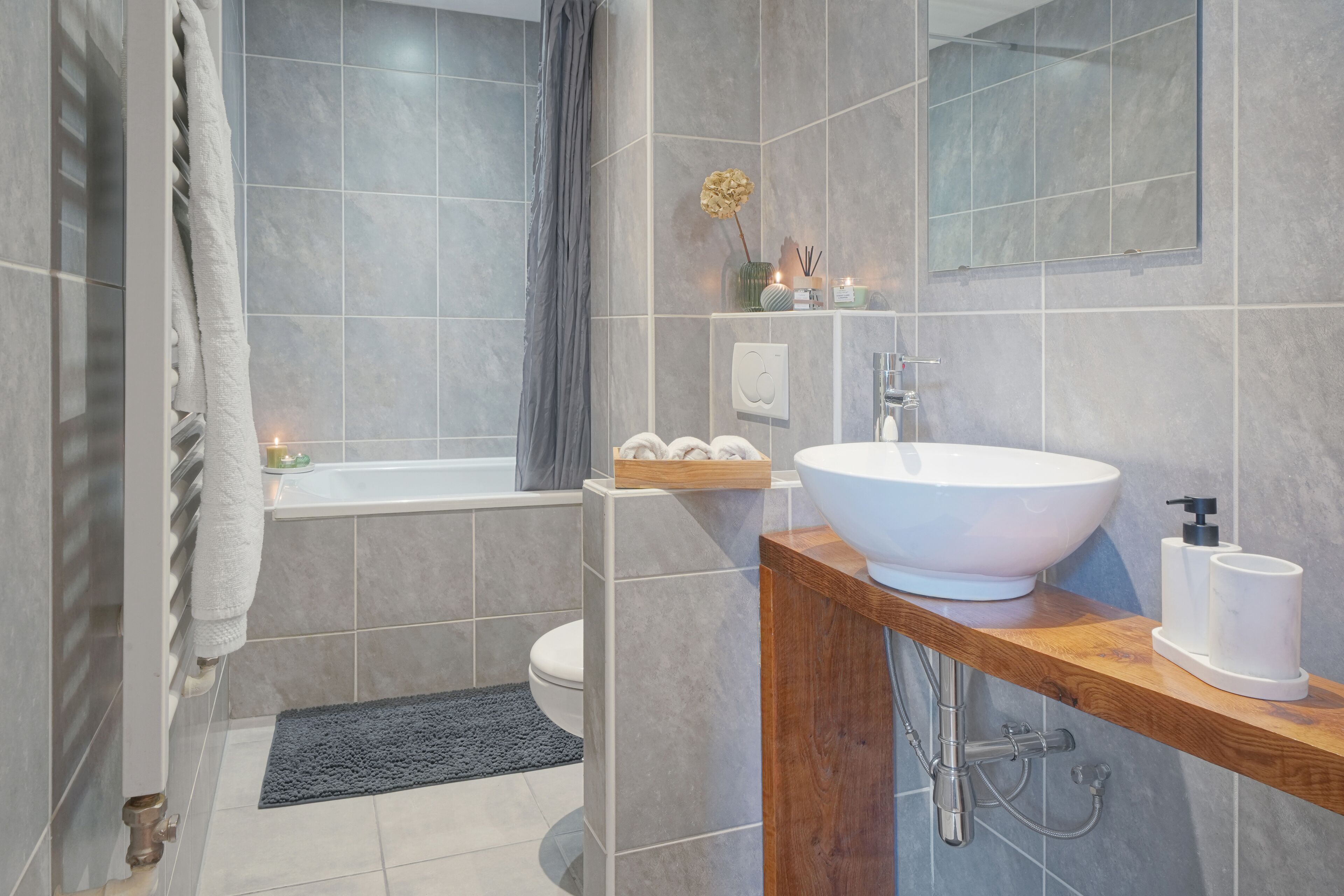 A modern bathroom with a large white sink, a wooden vanity, a bathtub, and a toilet.