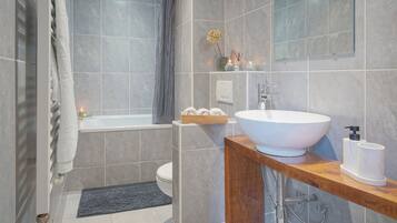 A modern bathroom with a large white sink, a wooden vanity, a bathtub, and a toilet.