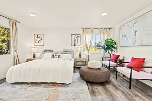 A modern bedroom with a large bed, bedside tables, a seating area with a chair and ottoman, and artwork on the walls. - Near Dtla Gem Stylish Private Suite w King bed (Monterey Park)
