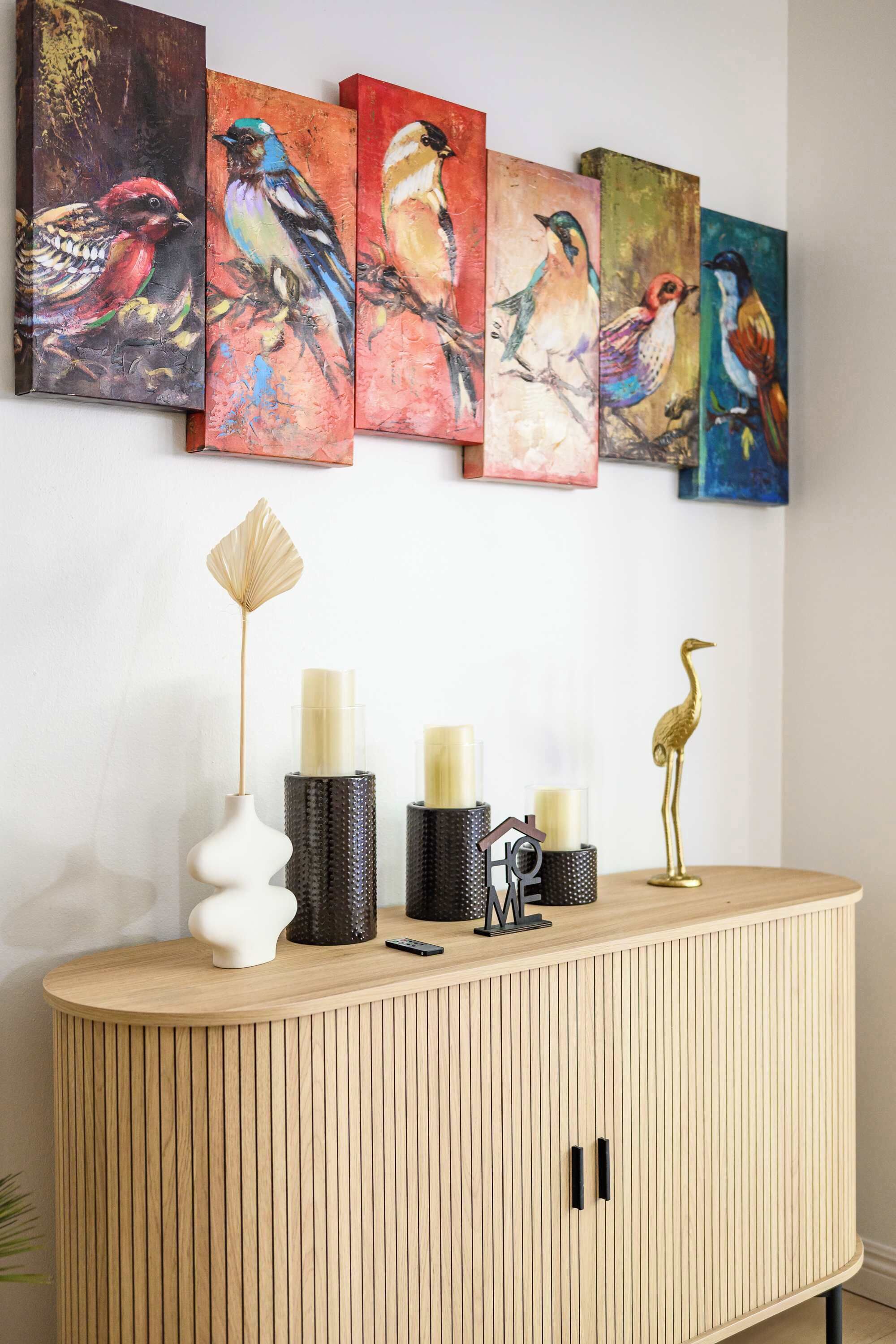 A wooden cabinet with a vase, candles, and a decorative bird.