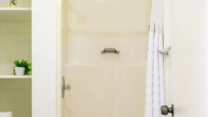 Ein Badezimmer mit Toilette, einer Dusche mit weißem Vorhang und einem Regal mit Pflanze und Pflegeprodukten.