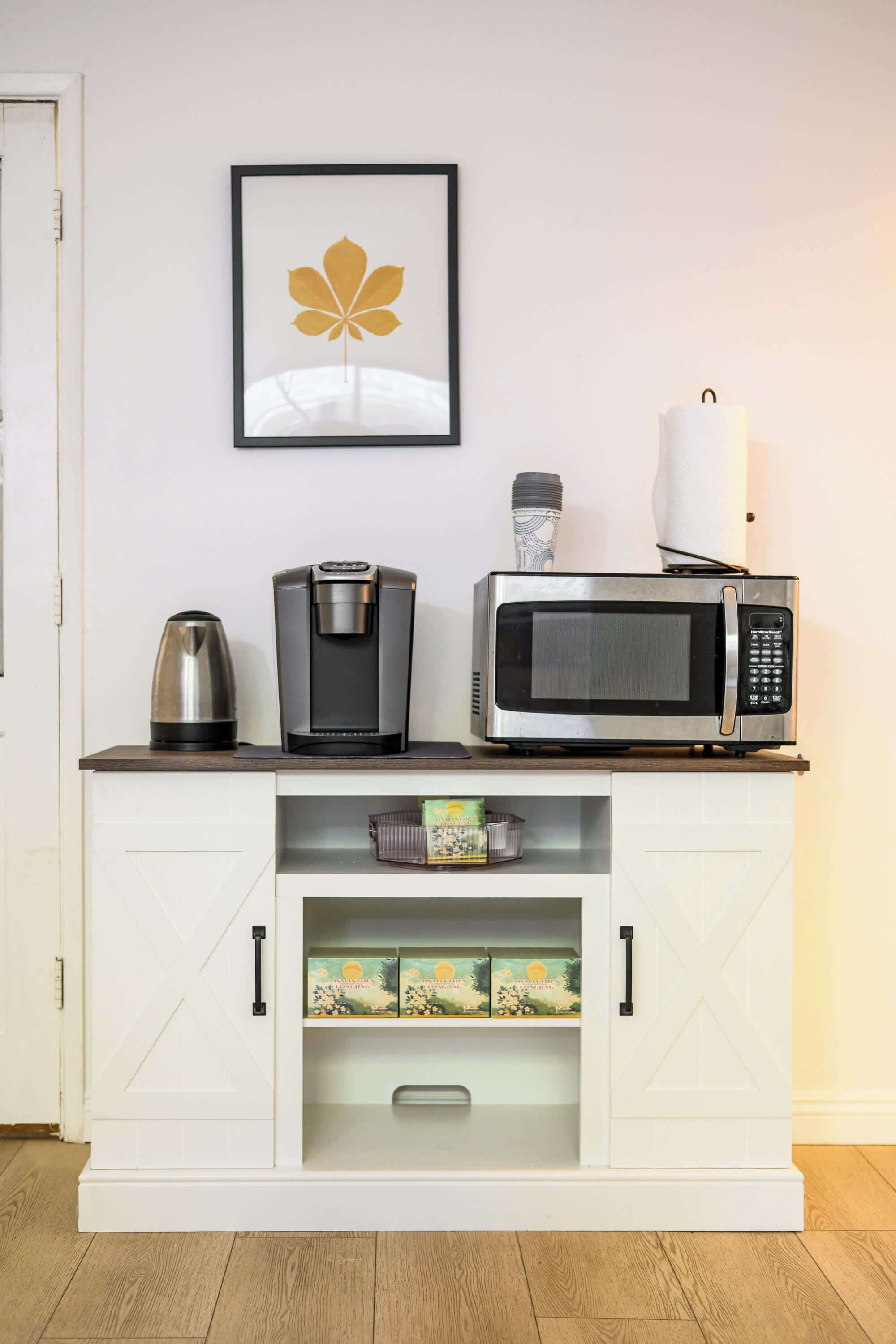 A kitchenette with a coffee maker, microwave, and a framed picture on the wall.
