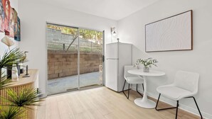 Ein modernes Zimmer mit einer Schiebetür zu einer Ziegelterrasse, einem weißen Kühlschrank, einem kleinen weißen Tisch mit zwei Stühlen und einem Topfpflanzen.