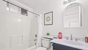 A modern bathroom with a white toilet, a bathtub, a sink with a vanity, a framed mirror, and a small potted plant. - Modern Hotel-style Suite in Monterey Park Near LA (Monterey Park)