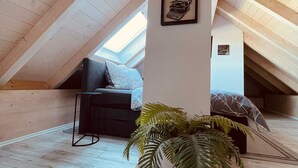 An attic room with a sloped ceiling, a black sofa, a potted plant, and a framed picture on the wall. - Allgäunest Apartment with Mountain View, Private Terrace and Wi-Fi (Argenbühl)