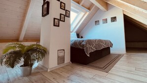 A bedroom with a sloped ceiling, a bed, a potted plant, and framed pictures on the wall. - Allgäunest Apartment with Mountain View, Private Terrace and Wi-Fi (Argenbühl)