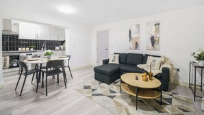 A modern living room with a dark sectional sofa, a round coffee table, and a dining area with a white table and black chairs. - Shirland Road Flat (London)