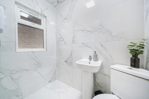 Een badkamer met witte marmeren tegels, een raam met baksteenmotief, een wastafel en een toilet.