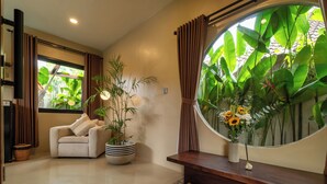A modern living room with a large window, a sofa, a coffee table, and a potted plant. - Lux Villa With Outdoor Pool & Garden (Bali)