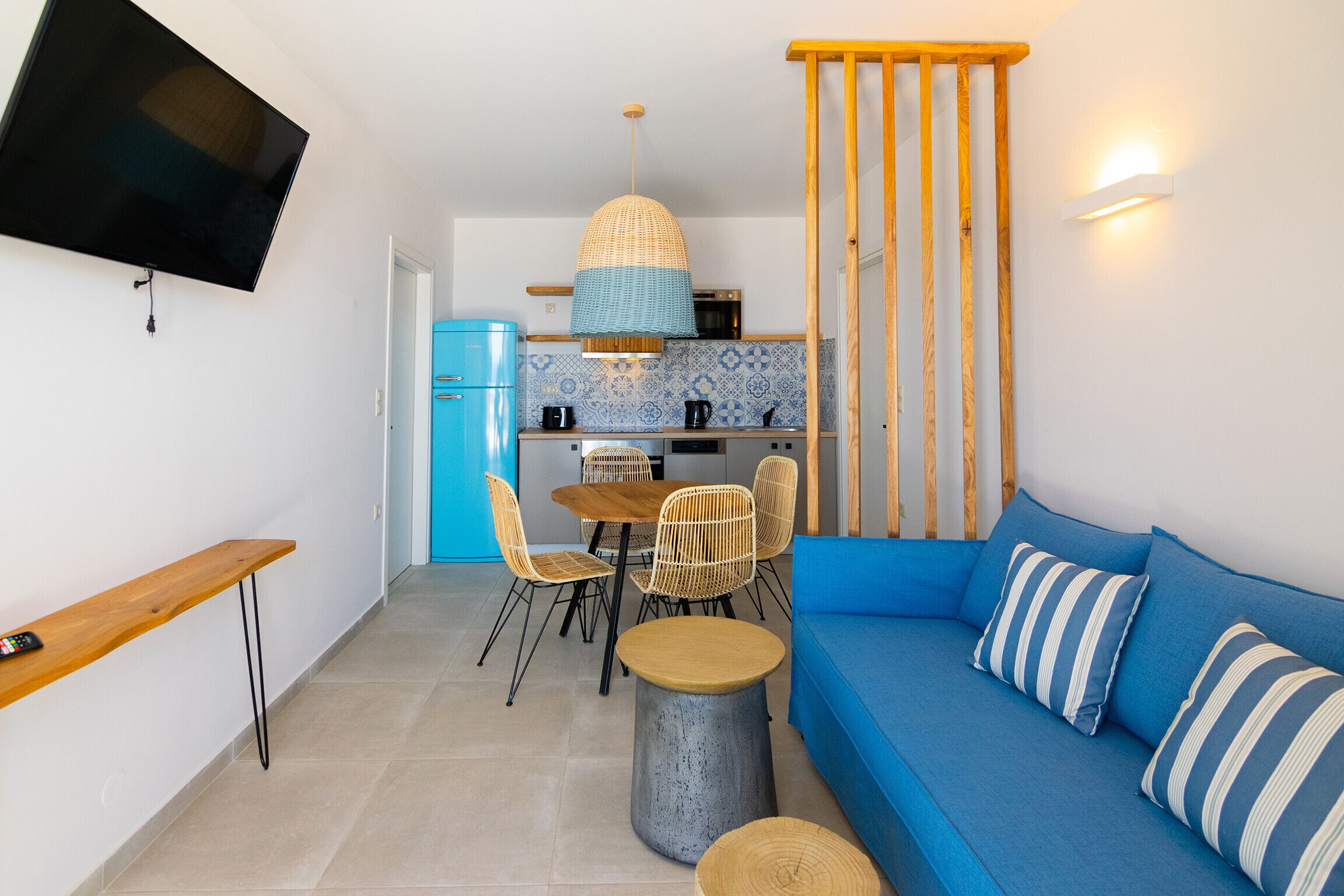 A compact living space with a kitchenette, a dining area with chairs, a sofa with striped pillows, and a television mounted on the wall.