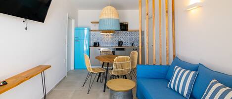 A compact living space with a kitchenette, a dining area with chairs, a sofa with striped pillows, and a television mounted on the wall.