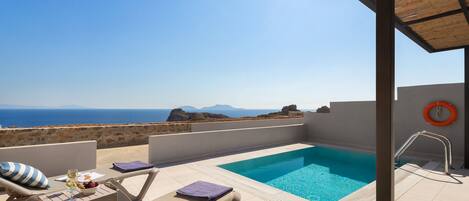 Une piscine sur le toit offrant une vue dégagée sur la mer, des chaises longues et une table avec une bouteille de vin.