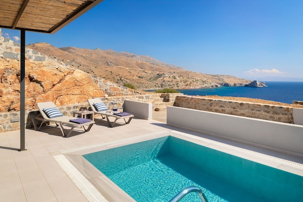 A pool with lounge chairs and a view of the sea and mountains.