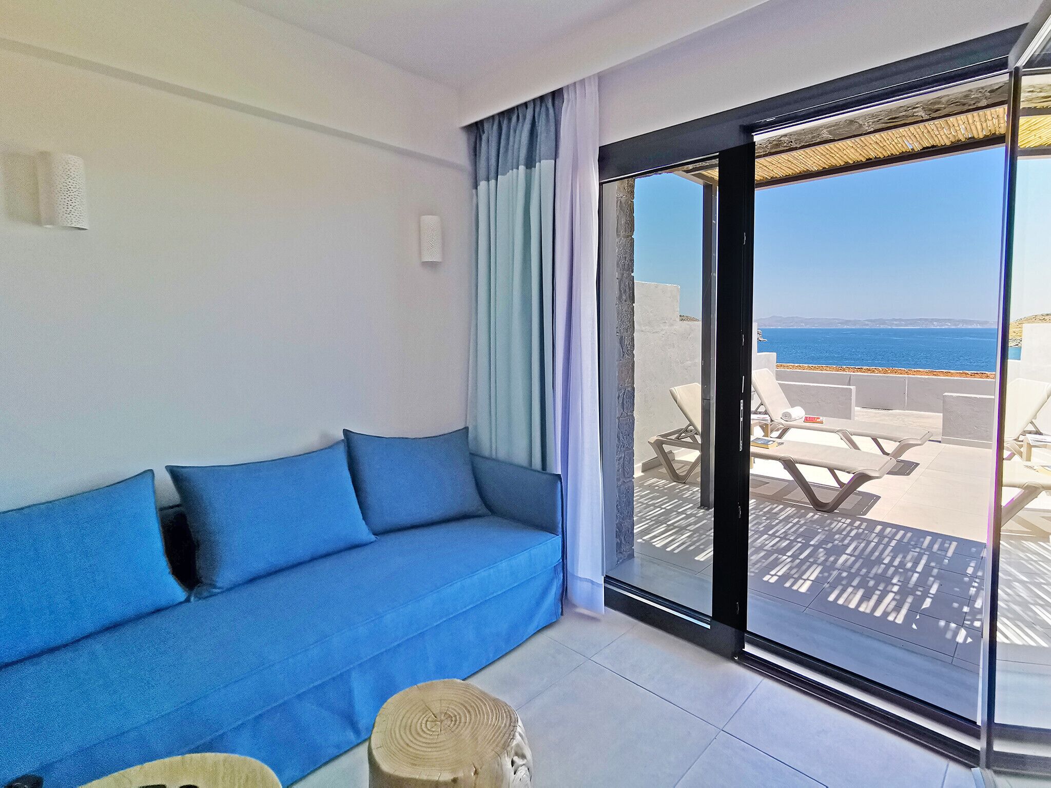 Une pièce avec un canapé bleu et une porte vitrée donnant sur un espace extérieur aménagé, avec vue sur la mer.