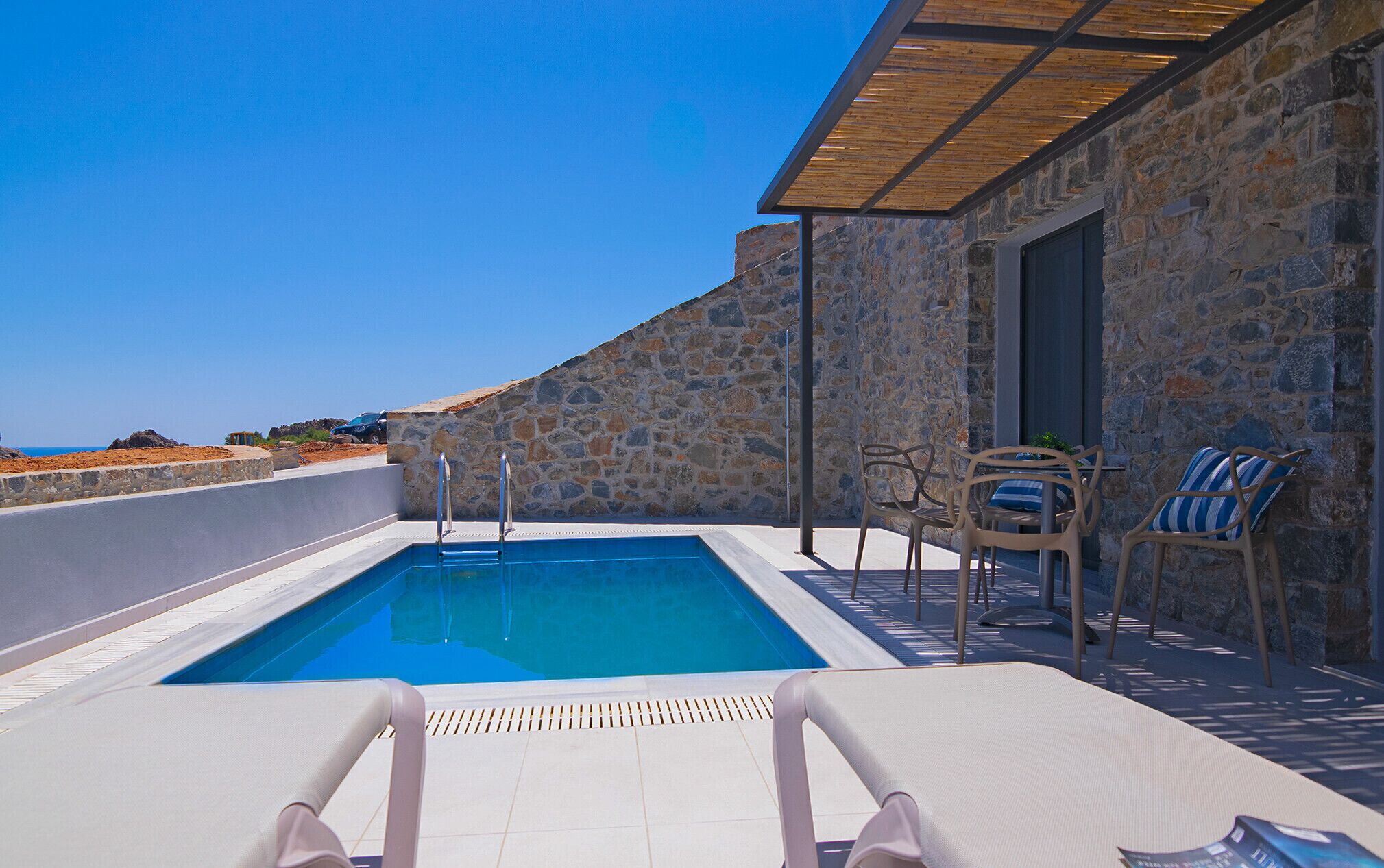 A pool area with stone walls, lounge chairs, and a view of the sea.