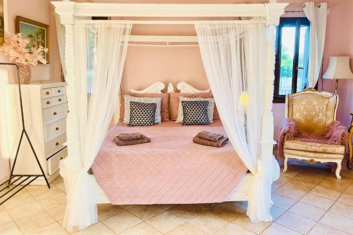 A four-poster canopy bed with a pink quilt, white curtains, and decorative pillows.