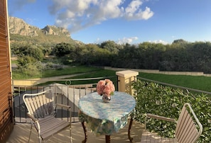 A balcony with a round table and two chairs, a vase with flowers, and a view of a mountainous landscape. - Esmaralda's House of Love (Terrasini)