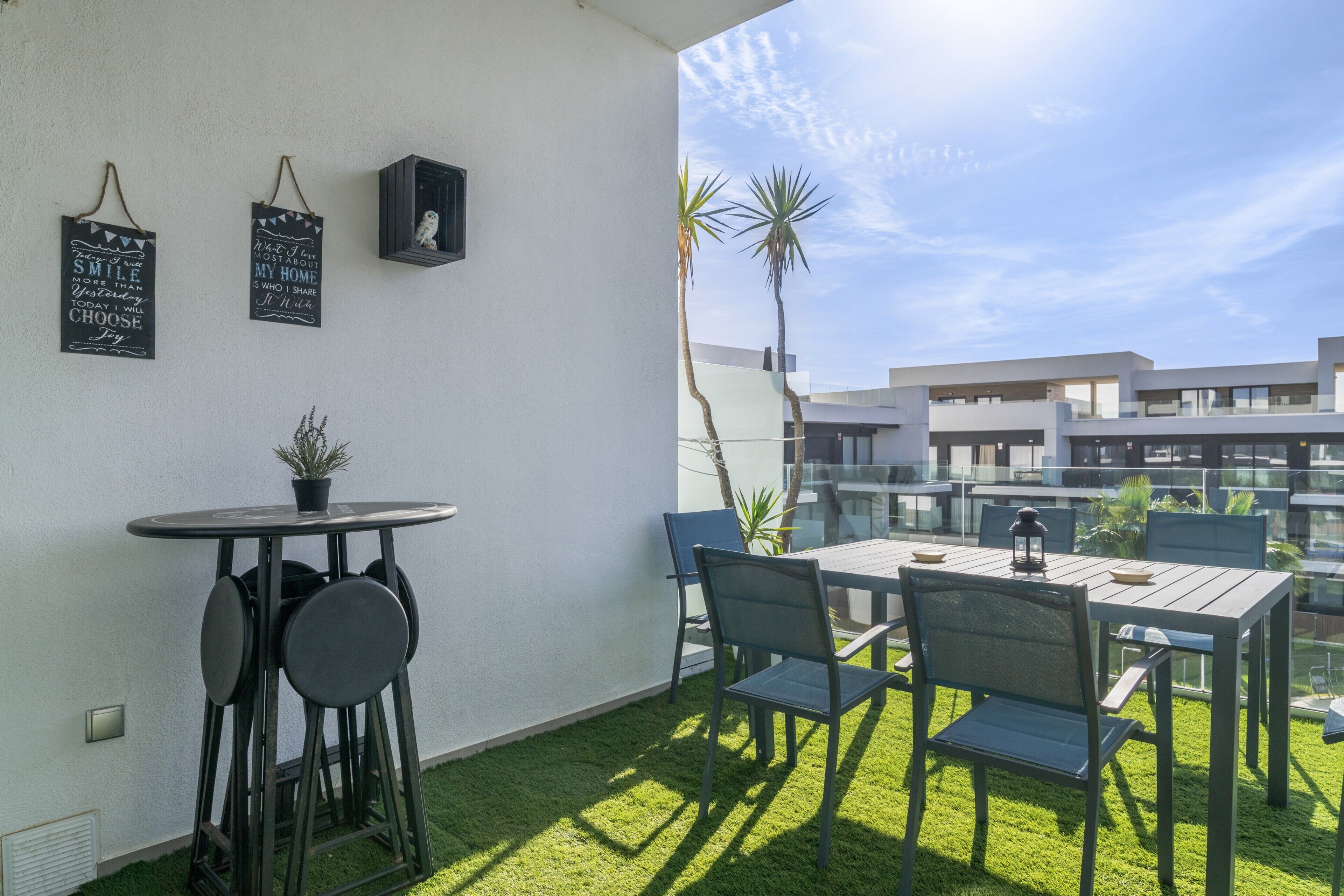 A balcony with a table and chairs, a small potted plant, and two wall decorations.
